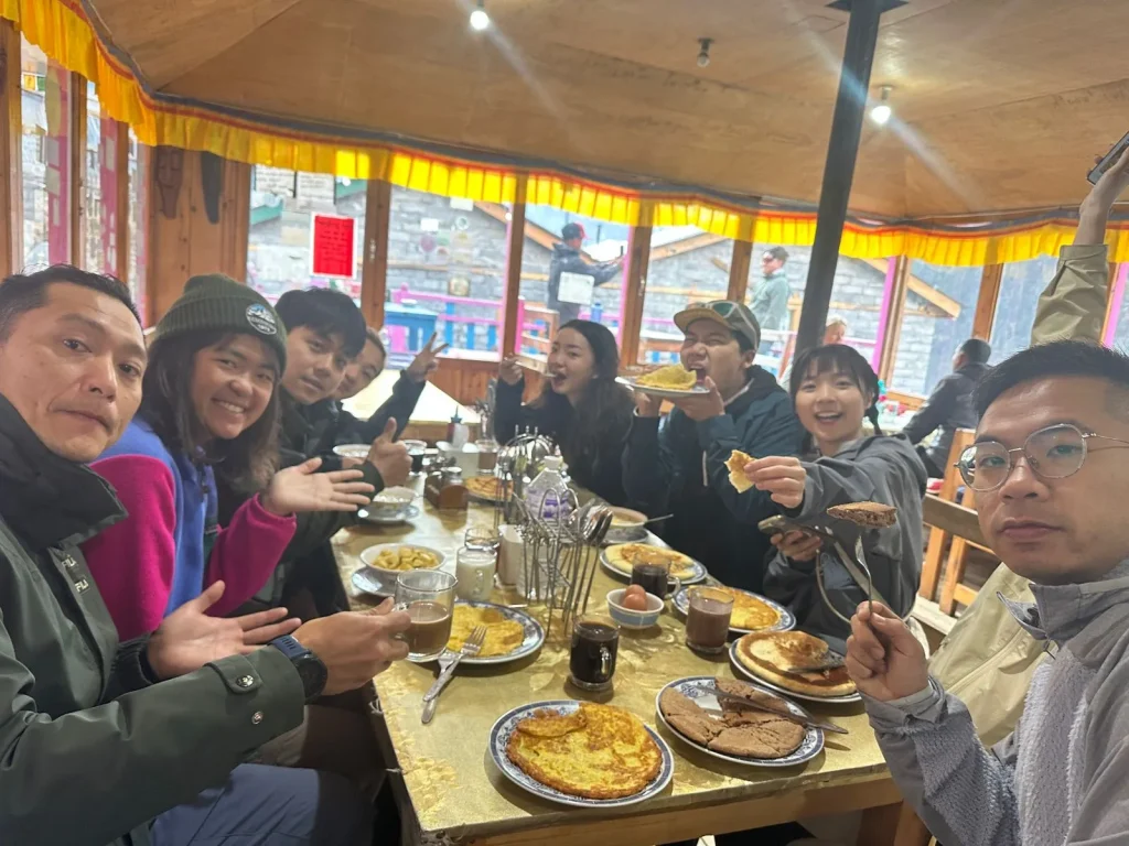 Trekkers enjoying breakfast with pancakes, eggs, and tea at a teahouse during the Annapurna Circuit trek in Nepal