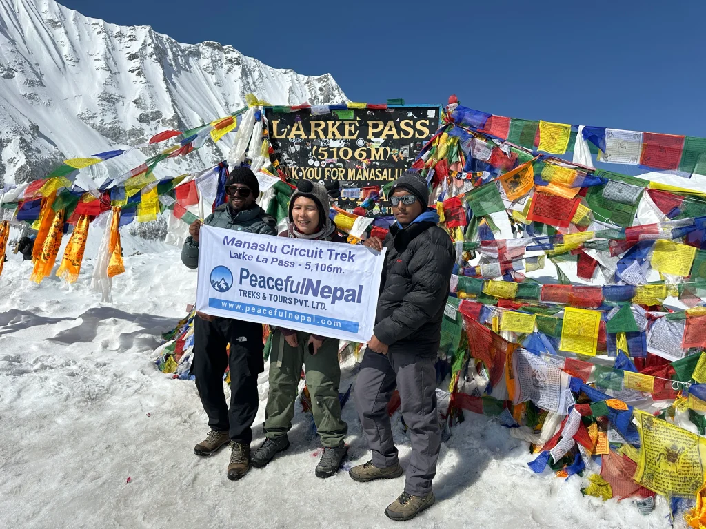 Trekkers at Larke Pass (5,106 m) with prayer flags and snowy peaks.