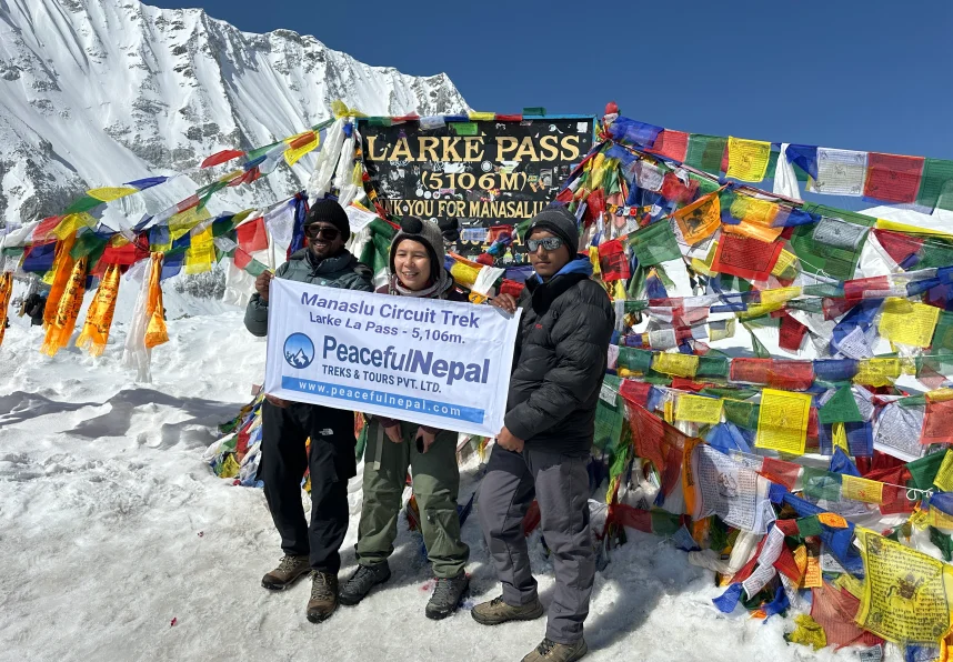 Trekkers at Larke Pass (5,106 m) with prayer flags and snowy peaks.