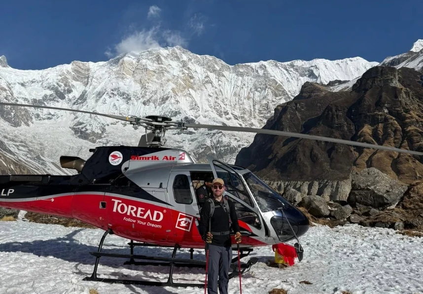 Trekker standing beside a helicopter at Annapurna Base Camp with snow-covered Annapurna mountains in the background, Nepal.
