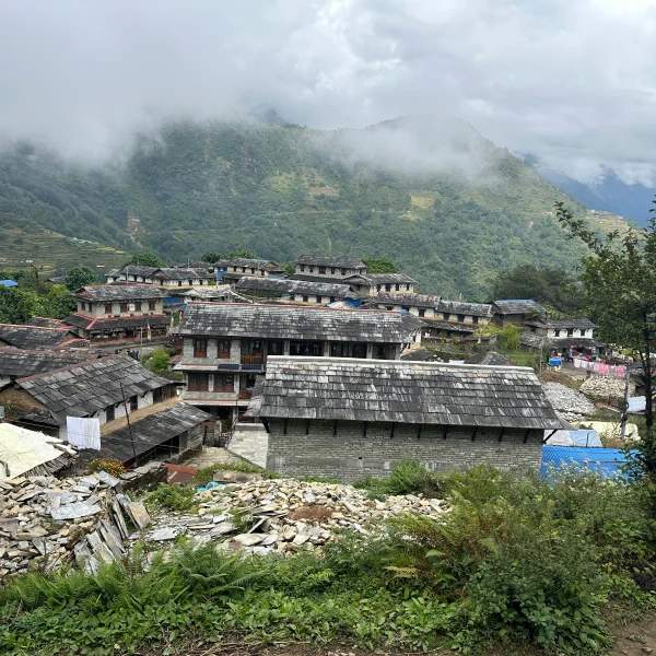 Traditional stone houses in Ghandruk Gurung village with green hills and misty mountains in the Annapurna region of Nepal.