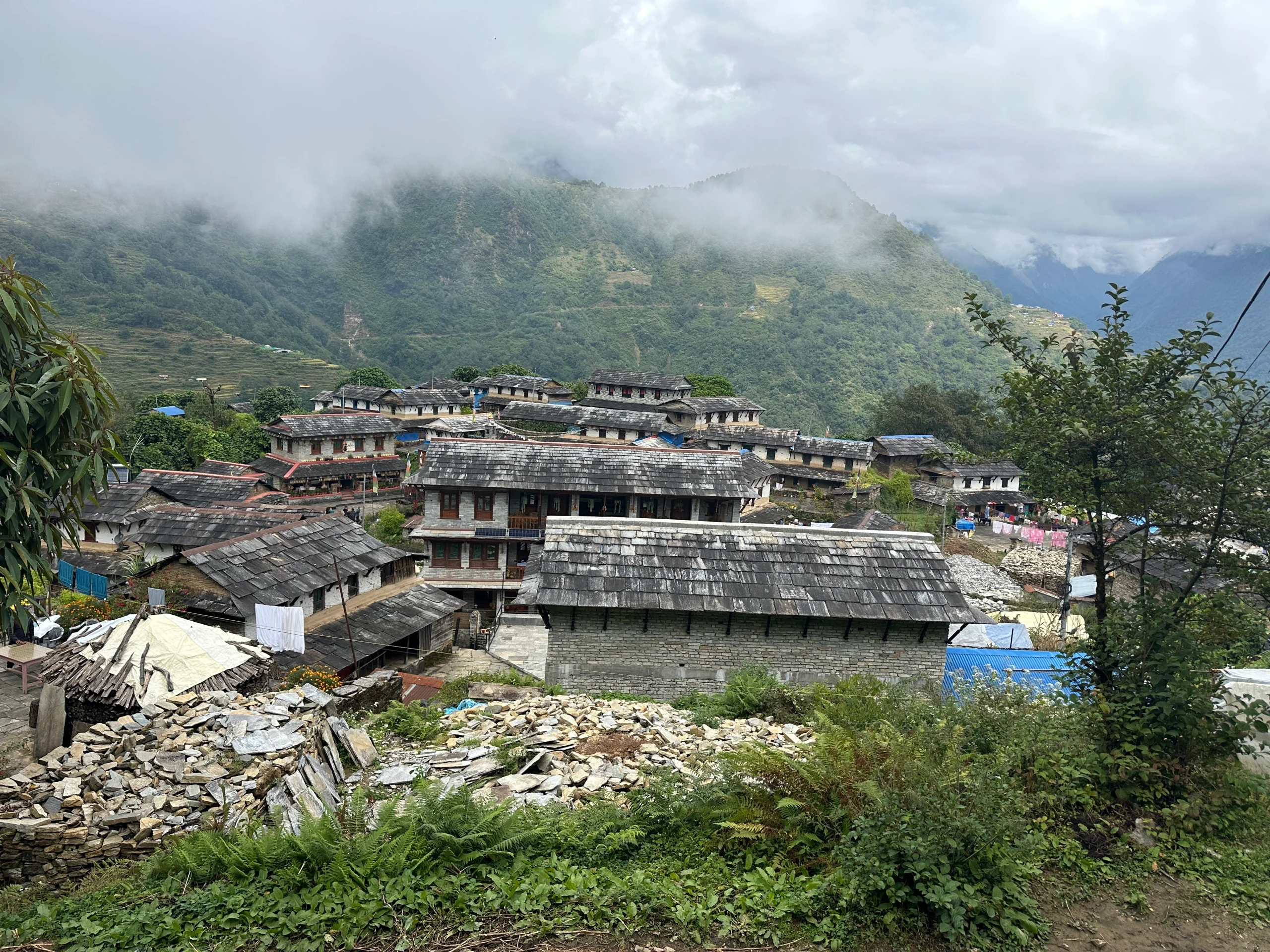 Traditional stone houses in Ghandruk Gurung village with green hills and misty mountains in the Annapurna region of Nepal.