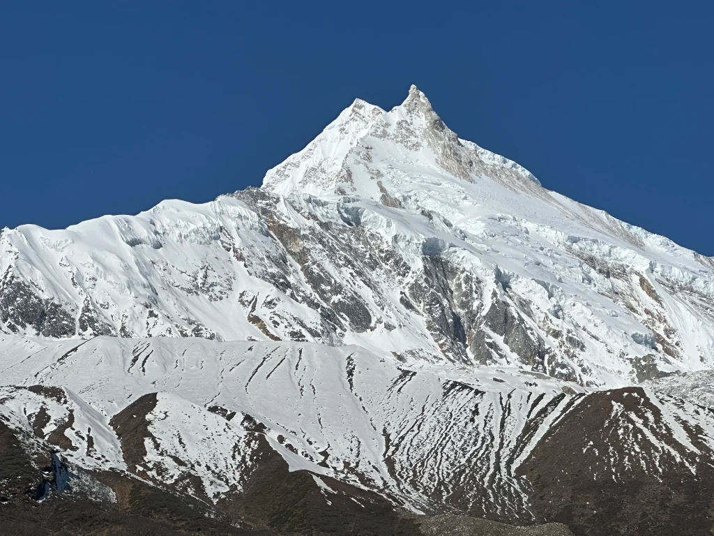 Manaslu Circuit Trek vs Annapurna Circuit Trek: Snow-covered Mount Manaslu rising above rugged Himalayan ridges under a clear blue sky in Nepal.